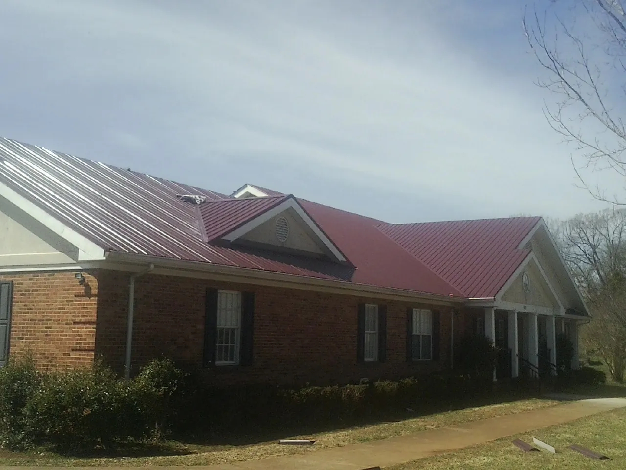 Red metal roof with gabled entries on a long brick building, from a Hail Damage Roof Repair job in Lodi