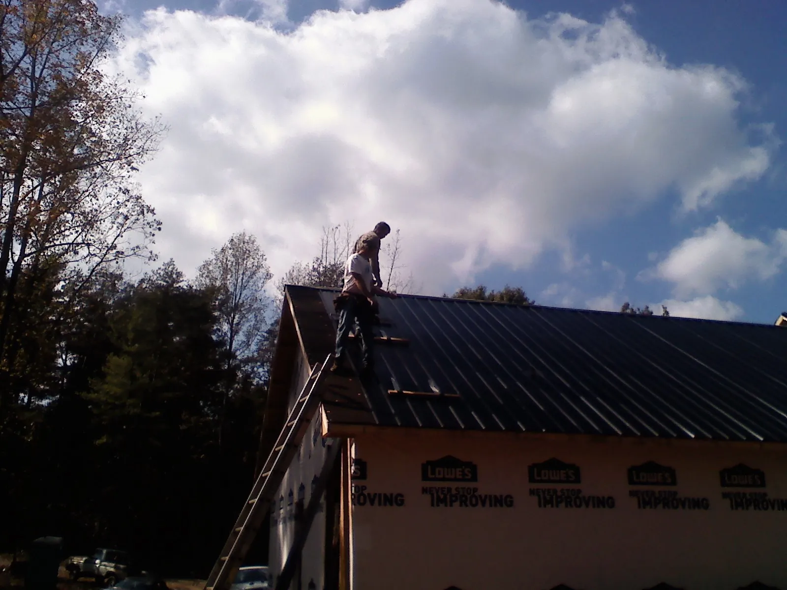 Roofer fastening dark metal panels high against a cloudy sky, from a Roof Inspection job in Lodi