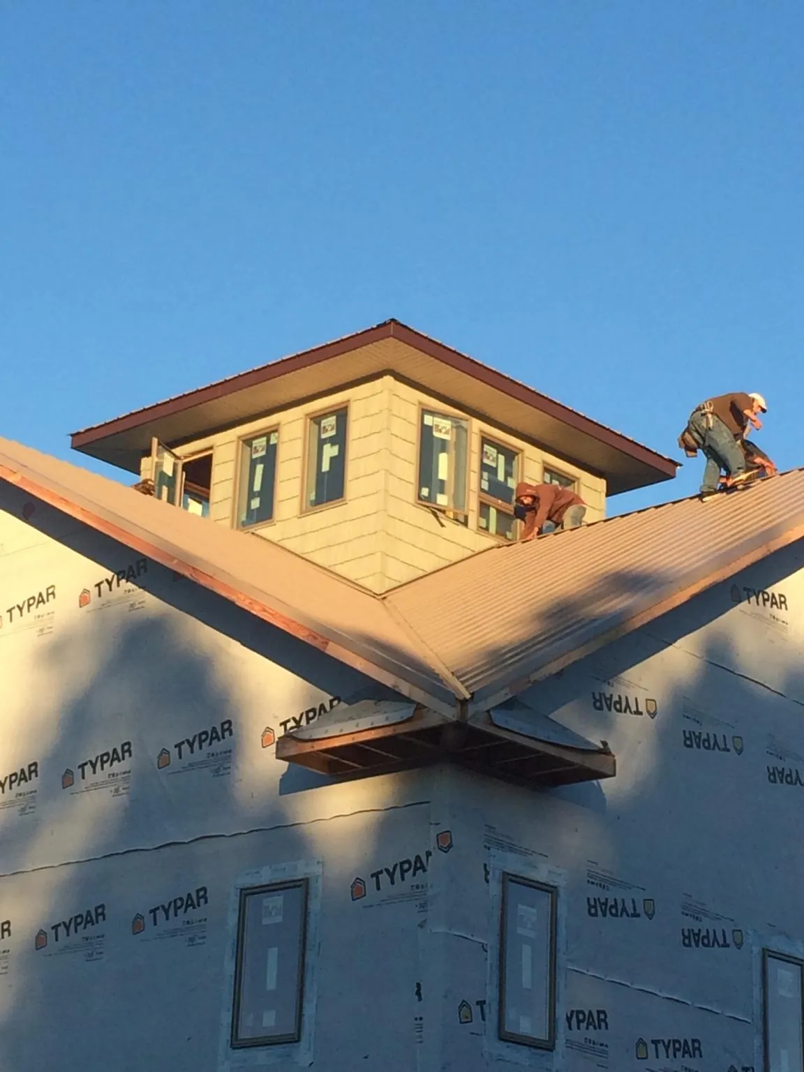 Roofers working around a rooftop cupola on a new metal roof at sunset in Lodi